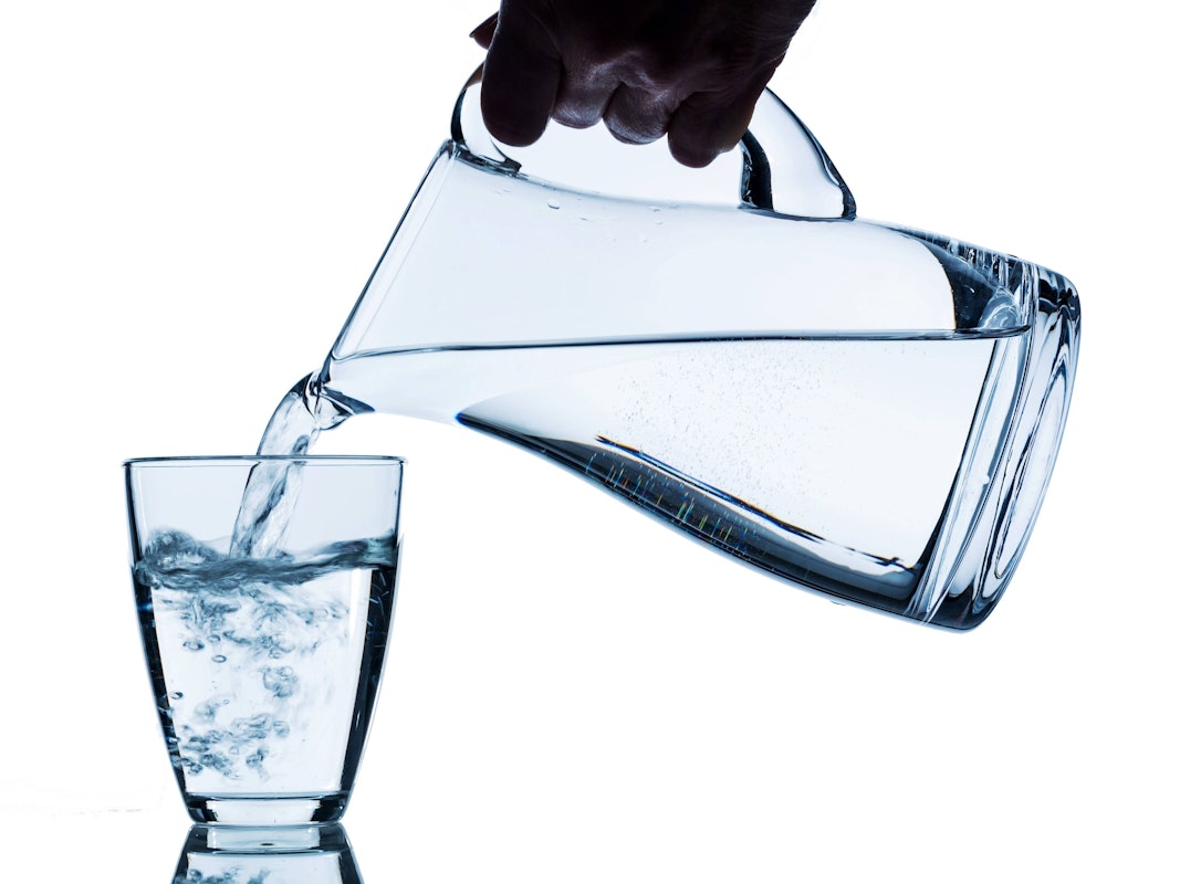 Reines Wasser wird in ein Wasserglas aus einem Krug gegossen.