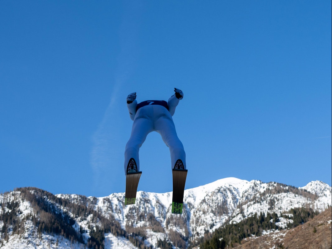 Ein Skispringer kurz nach dem Absprung, von unten und hinten fotografiert.
