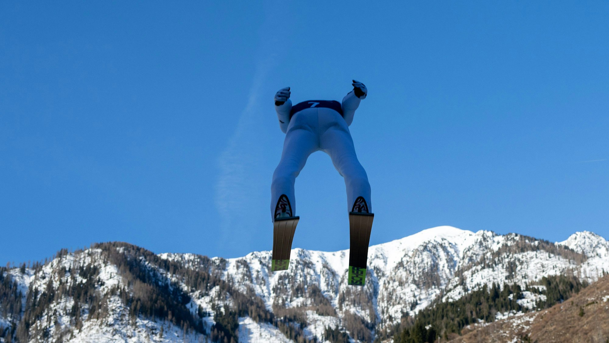 Ein Skispringer kurz nach dem Absprung, von unten und hinten fotografiert.