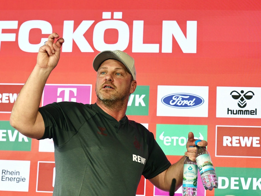 Lukas Kwasniok (1. FC Köln) trägt zwei Wasserflaschen vom Podium.