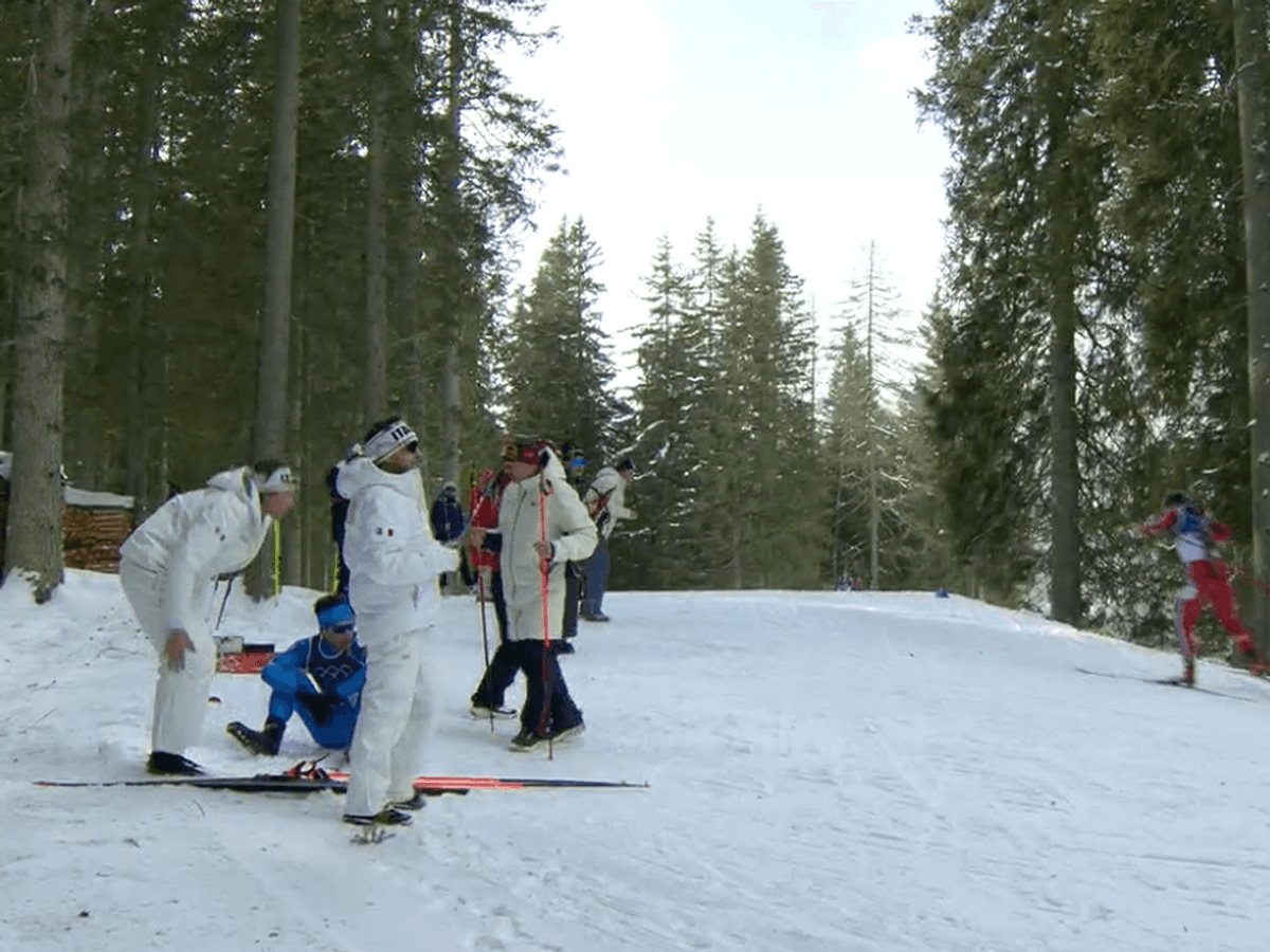 Tommaso Giacomel sitzt erschöpft im Schnee. Um ihn herum Teambetreuer.