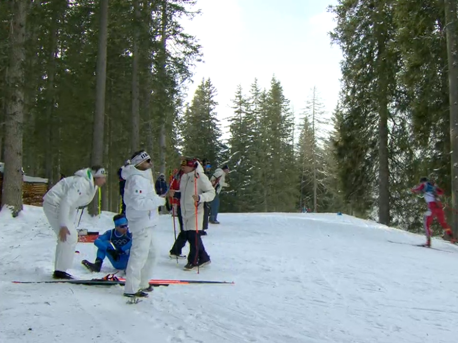 Tommaso Giacomel sitzt erschöpft im Schnee. Um ihn herum Teambetreuer.