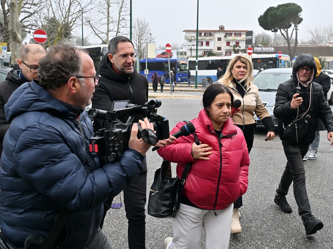 Eine Frau wird von Medienvertretern, unter anderem mit einer Kamera, umringt.