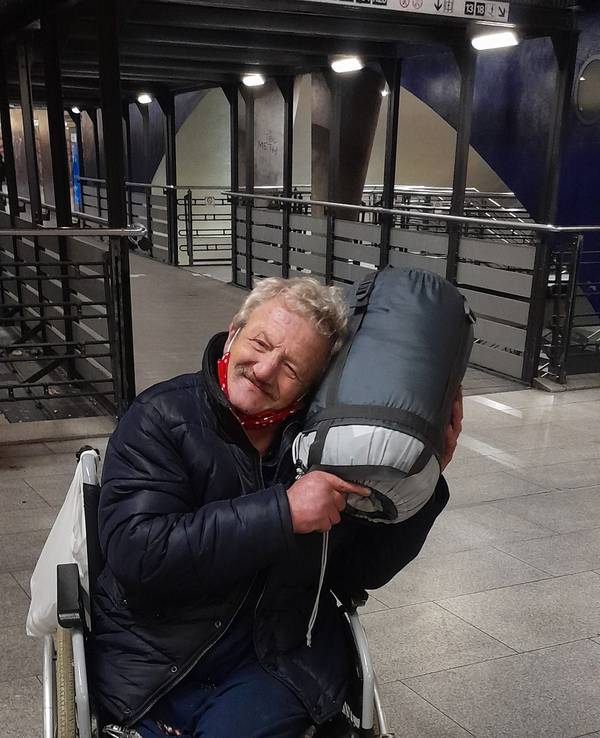 Ein Mann im Rollstuhl kuschelt mit einem aufgerollten Schlafsack.