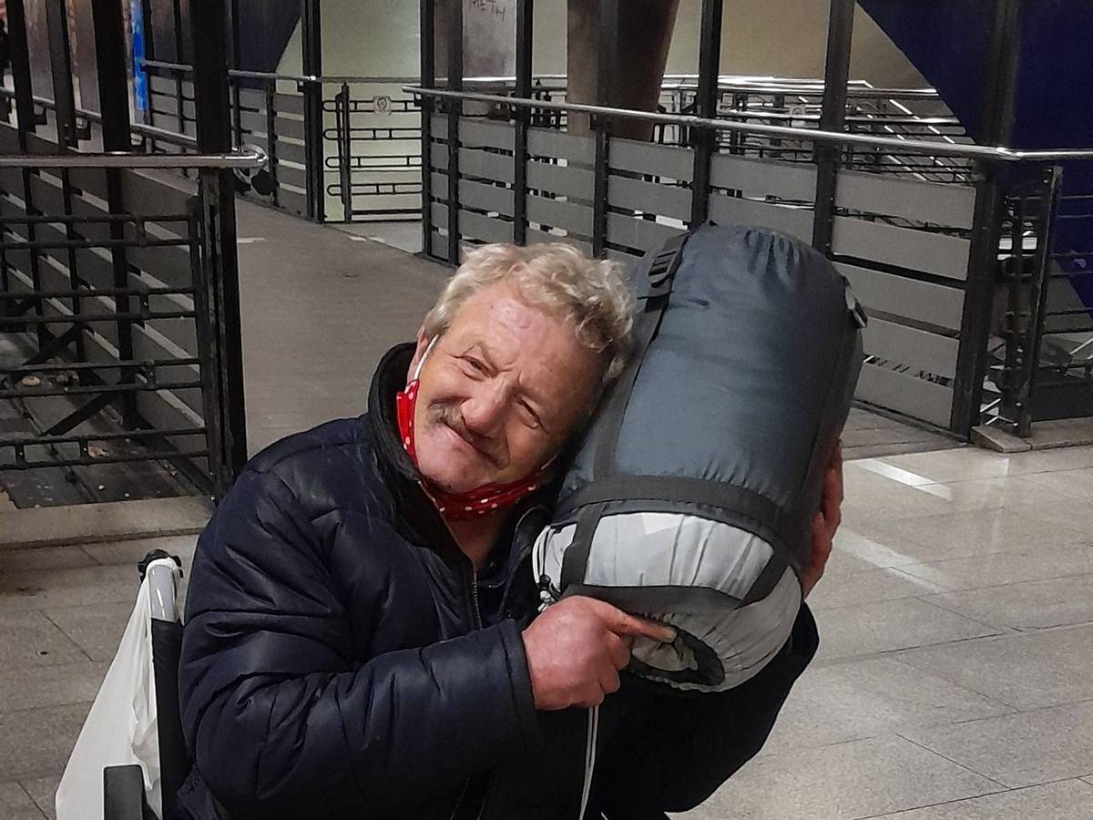 Ein Mann im Rollstuhl kuschelt mit einem aufgerollten Schlafsack.