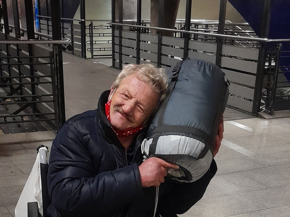 Ein Mann im Rollstuhl kuschelt mit einem aufgerollten Schlafsack.