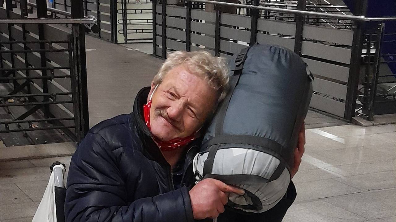 Ein Mann im Rollstuhl kuschelt mit einem aufgerollten Schlafsack.