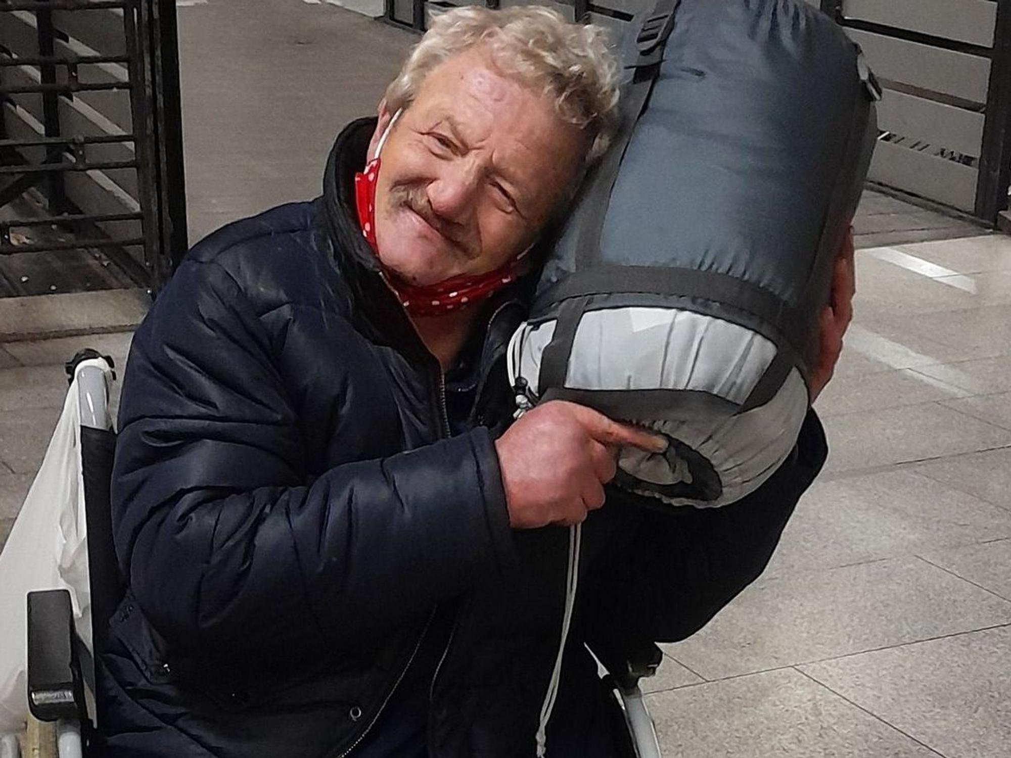 Ein Mann im Rollstuhl kuschelt mit einem aufgerollten Schlafsack.