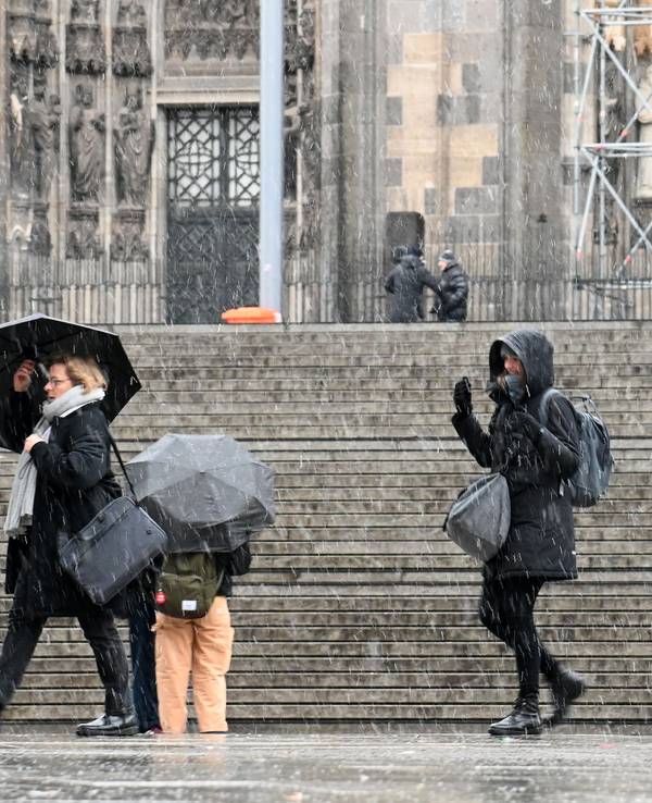 Menschen gehen bei Schneefall mit Regenschirmen am Kölner Dom vorbei.
