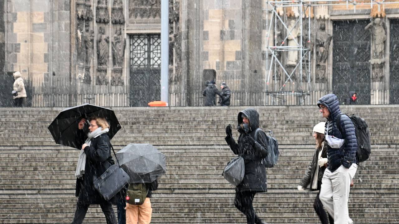 Menschen gehen bei Schneefall mit Regenschirmen am Kölner Dom vorbei.