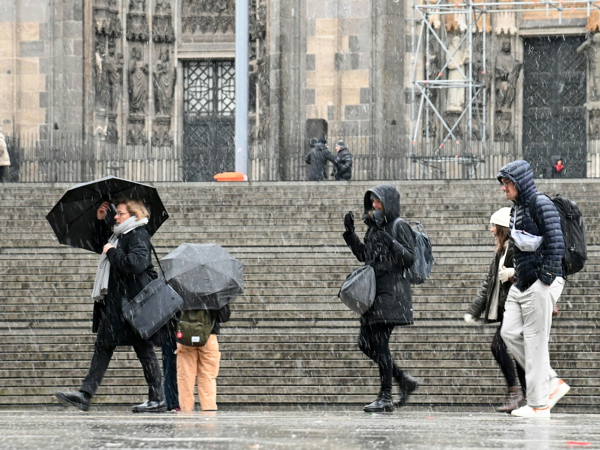 Menschen gehen bei Schneefall mit Regenschirmen am Kölner Dom vorbei.