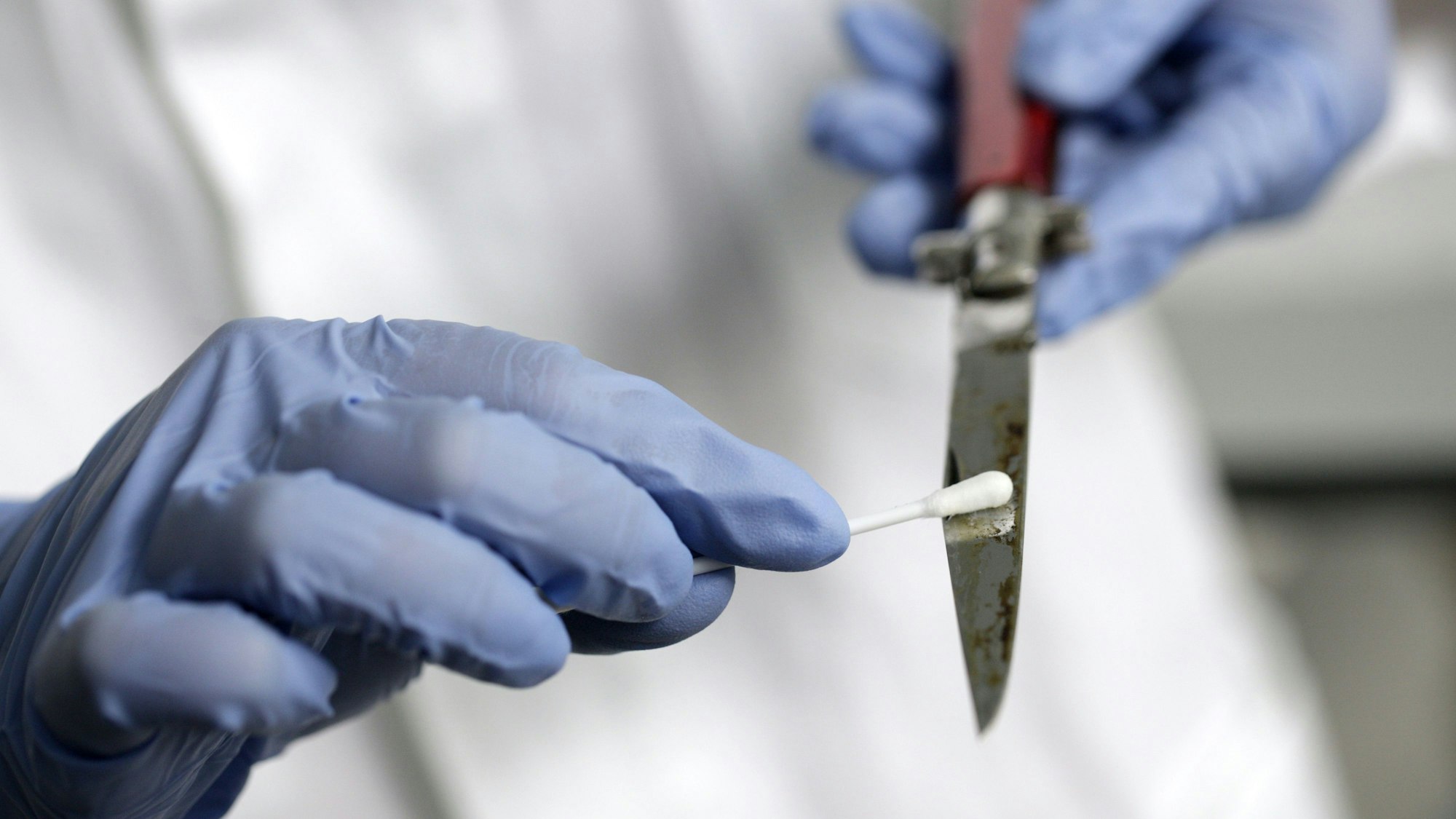 Eine Labormitarbeiterin streicht mit einem Q-Tip über die Klinge eines Messers.