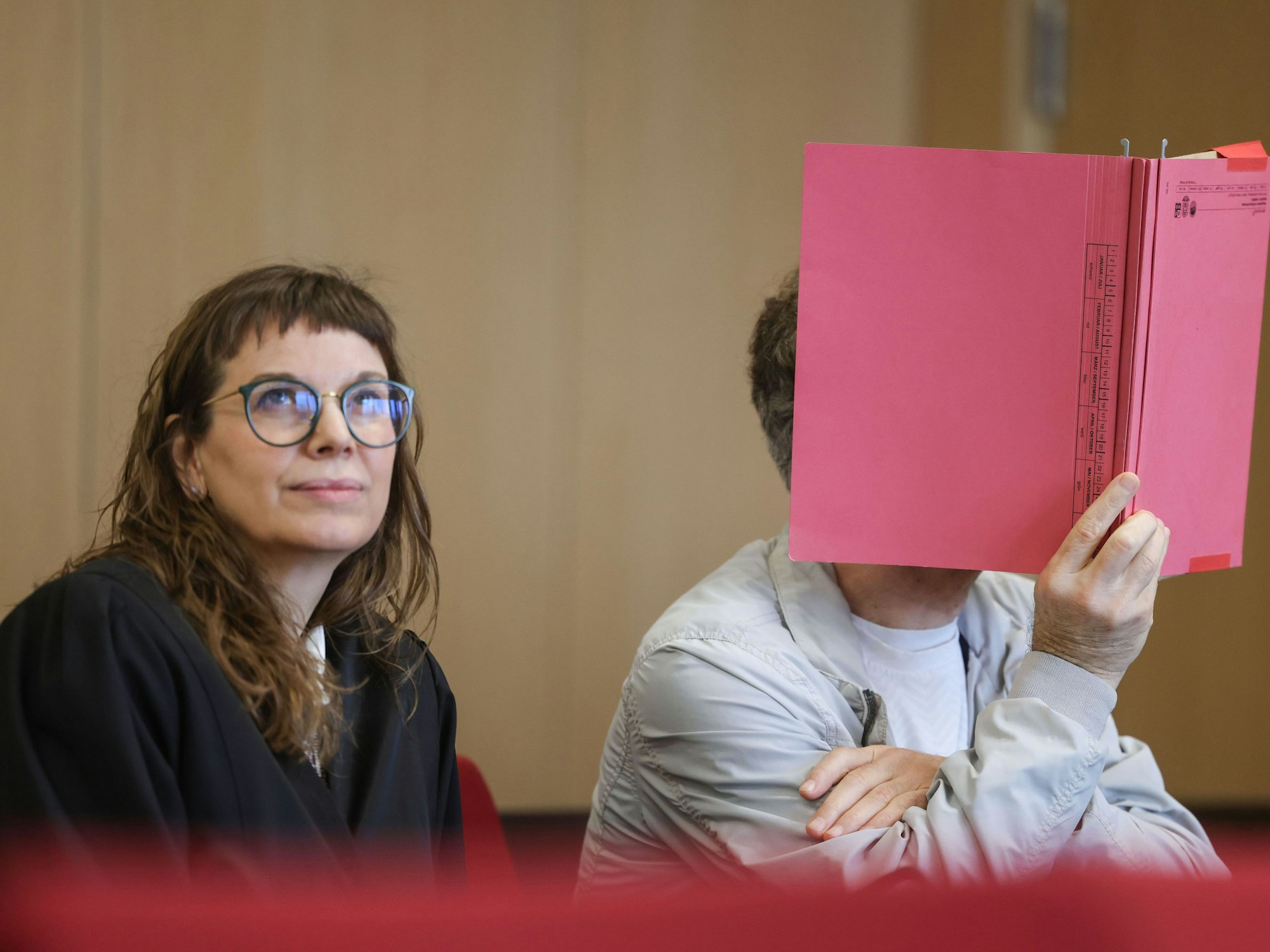 Rechtsanwältin Hannah Milena Piel (l) sitzt neben ihrem Mandanten, der sich einen Aktenordner vor das Gesicht hält, im Prozess um die Ermordung eines Professors im Jahr 1984 in Hilden. Der „Cold Case“ konnte nach Jahrzehnten durch einen DNA-Treffer aufgeklärt werden. Angeklagt ist ein 62-Jähriger Mann, der aus Italien an die deutsche Justiz ausgeliefert wurde.