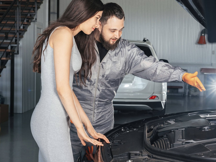 Automechaniker und Kundin vor offenem Automotor