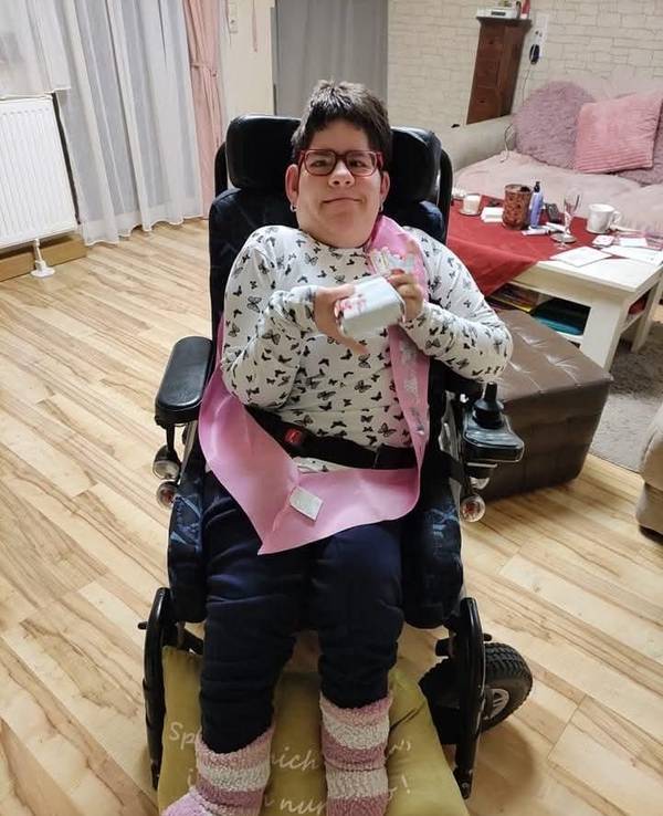 Die schwerbehinderte Maria sitzt in einem Stuhl und grinst in die Kamera.