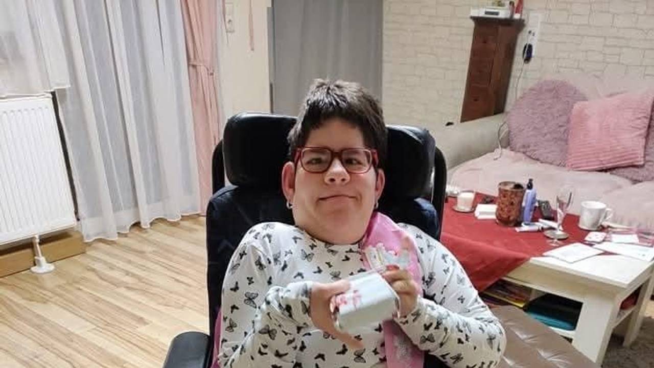 Die schwerbehinderte Maria sitzt in einem Stuhl und grinst in die Kamera.
