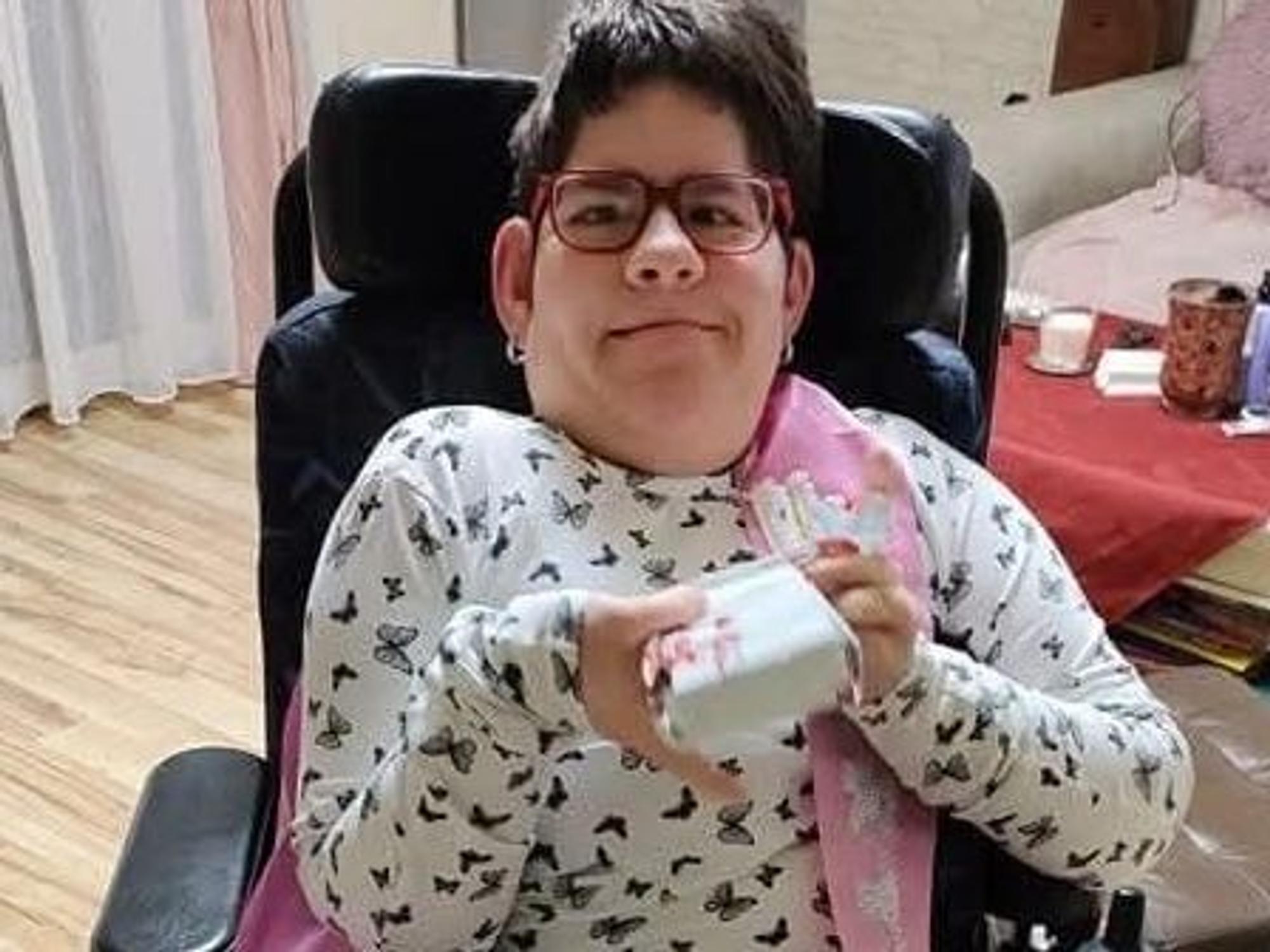Die schwerbehinderte Maria sitzt in einem Stuhl und grinst in die Kamera.