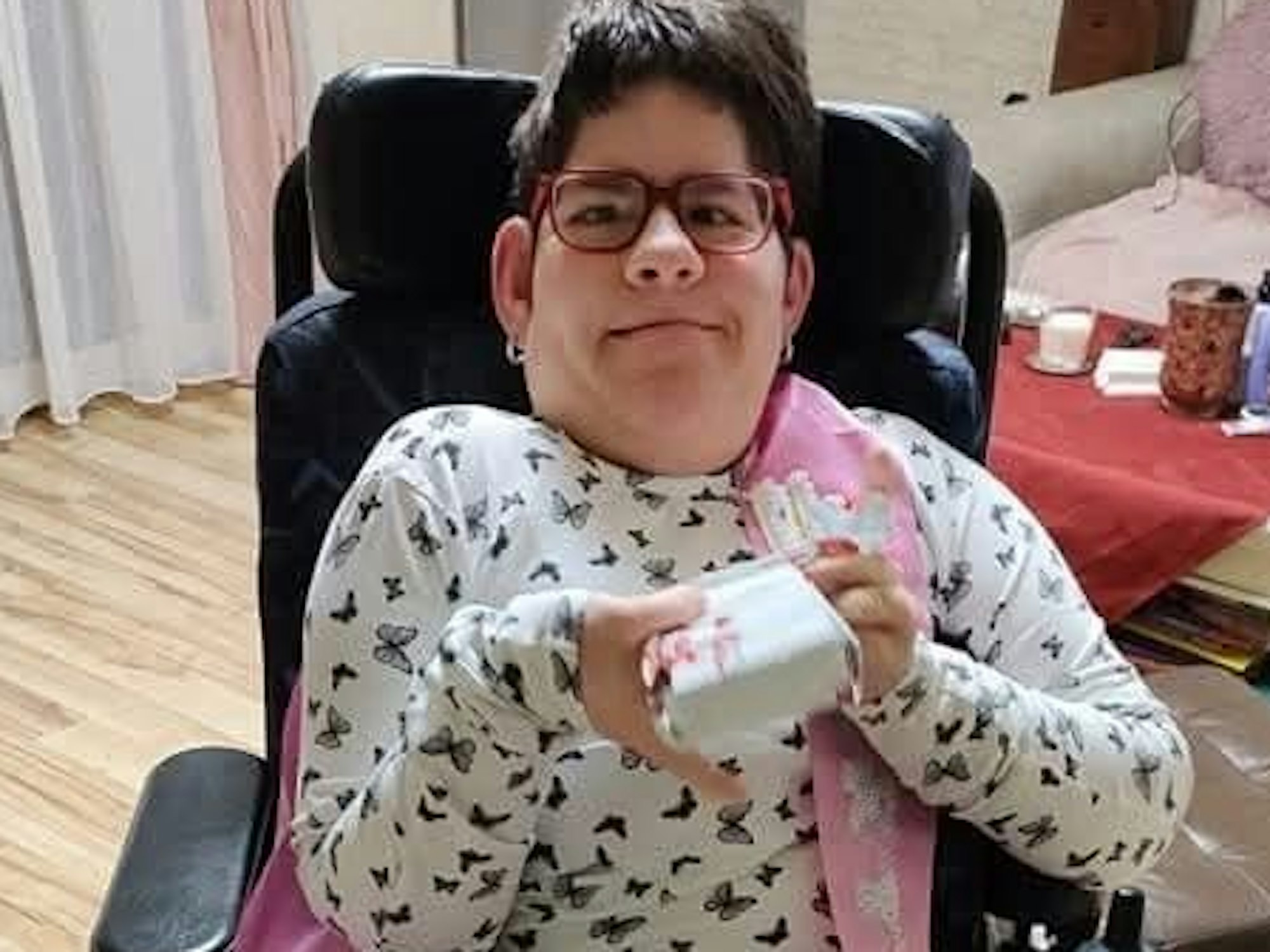 Die schwerbehinderte Maria sitzt in einem Stuhl und grinst in die Kamera.