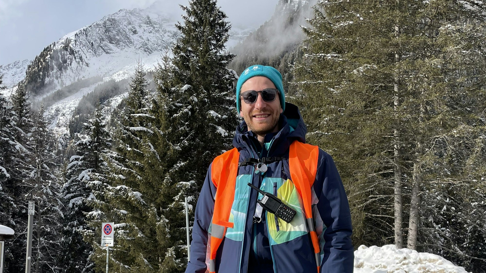 Der Olympia-Volunteer Niels Gietmann posiert mit Weste vor der Bergkulisse in Italien.