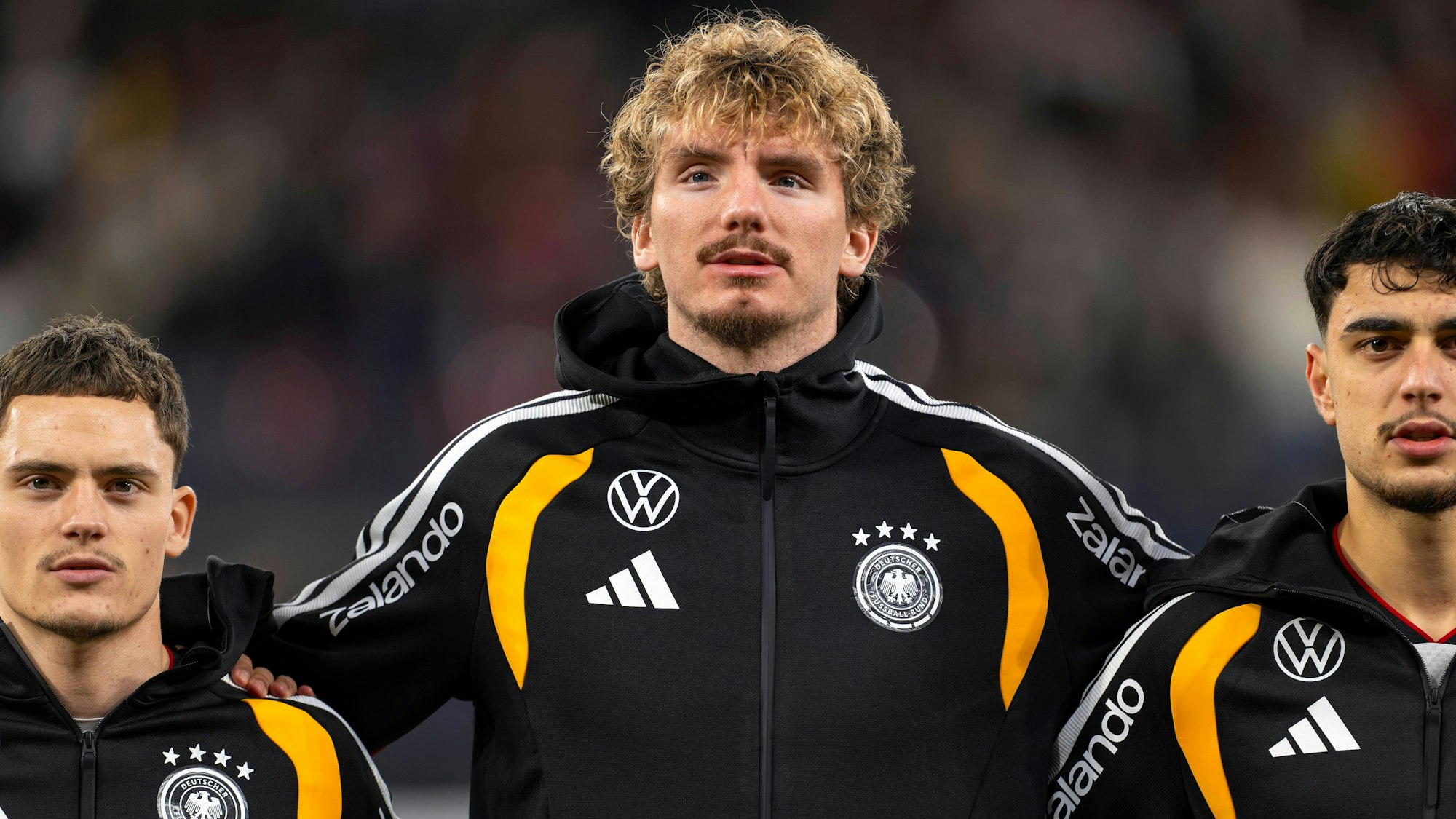 Florian Wirtz, Nick Woltemade und Aleksandar Pavlovic in schwarzer Trainingsjacke bei der Hymne.