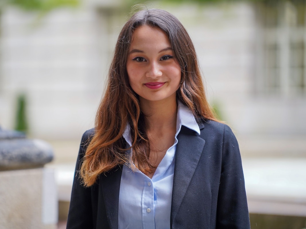 Eine junge Frau mit braunen, offenen Haaren, Bluse und Anzugjacke blickt freundlich in die Kamera