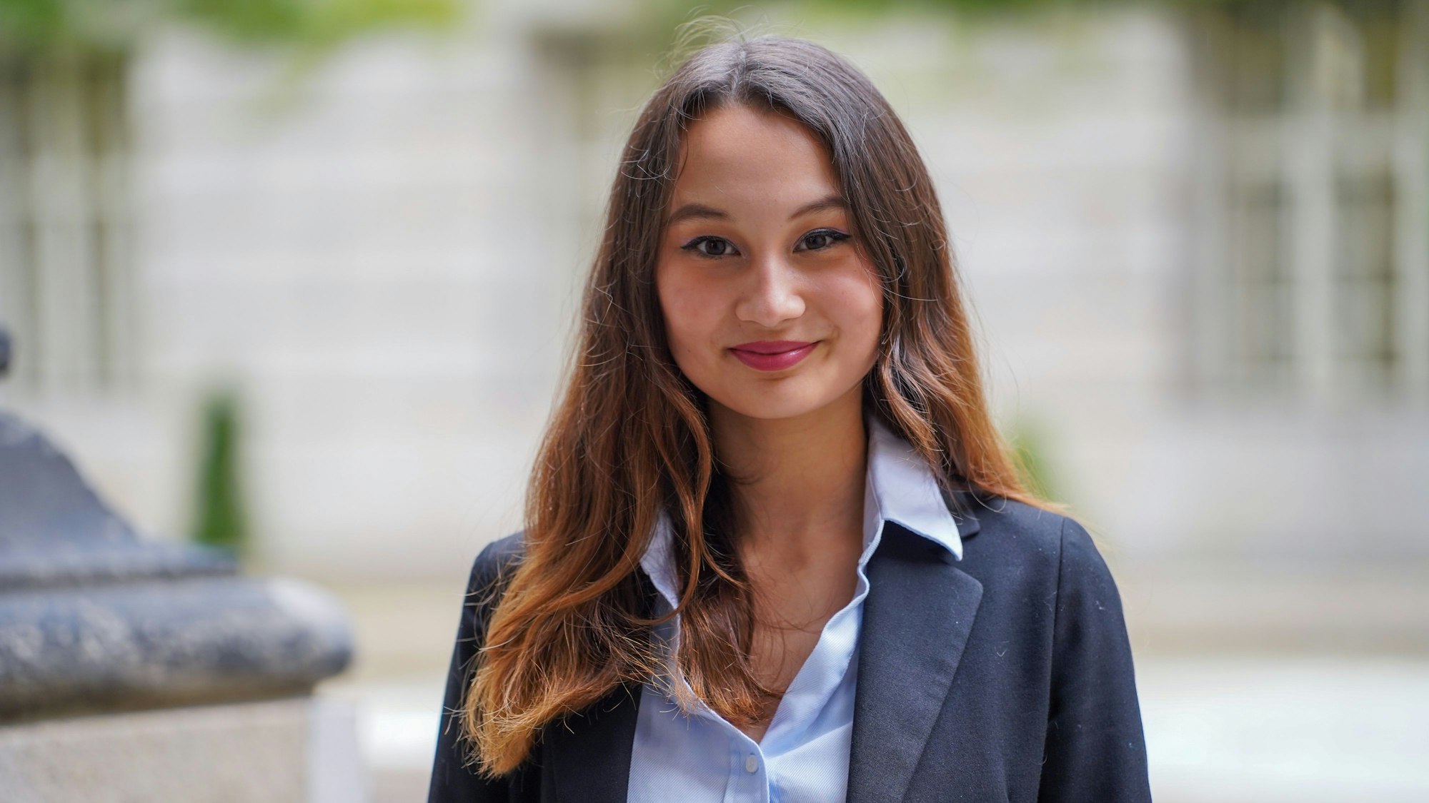 Eine junge Frau mit braunen, offenen Haaren, Bluse und Anzugjacke blickt freundlich in die Kamera