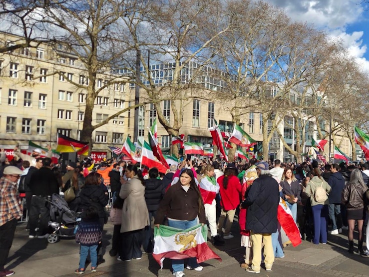 Menschen mit Iran-Flaggen drängen sich auf einem Platz.