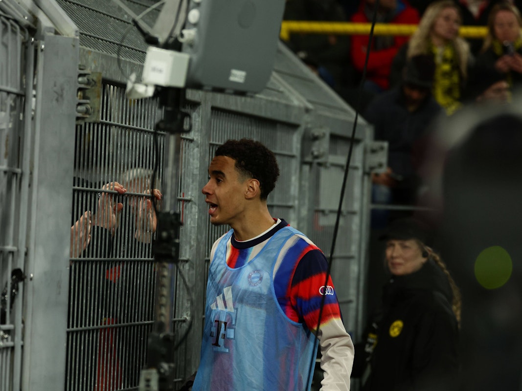 Jamal Musiala diskutiert mit Bayern-Fans hinter dem Zaun.