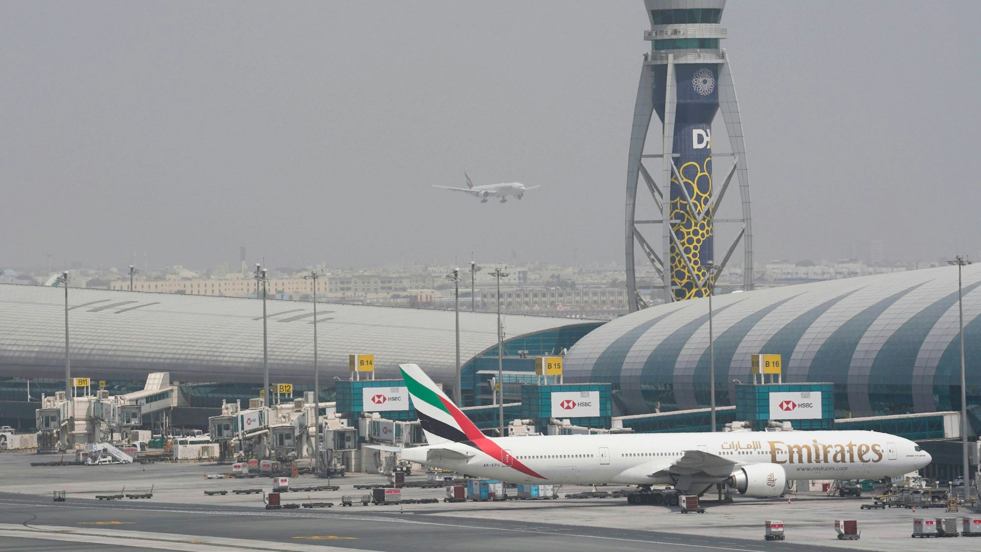 ARCHIV - 17.08.2022, Vereinigte Arabische Emirate, Dubai: ARCHIV - Eine Boeing 777 der Fluggesellschaft Emirates steht am Gate des internationalen Flughafens von Dubai, während sich eine andere Maschine auf die Landung auf der Startbahn vorbereitet. (zu dpa: «Angriff Irans? Verletzte nach «Vorfall» am Flughafen Dubai») Foto: Jon Gambrell/AP/dpa +++ dpa-Bildfunk +++
