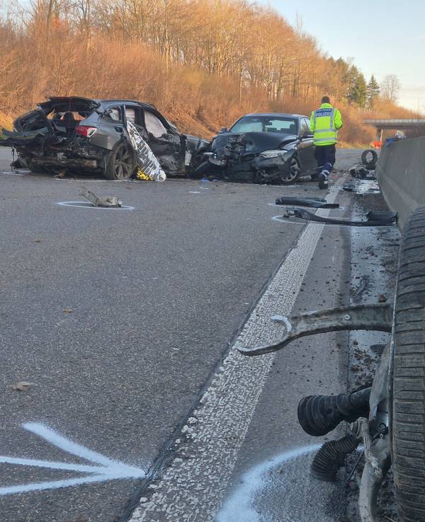 Ein Polizist geht nach einem Unfall auf der A1 an den verunglückten Fahrzeugen und zahlreichen Trümmerteilen entlang.