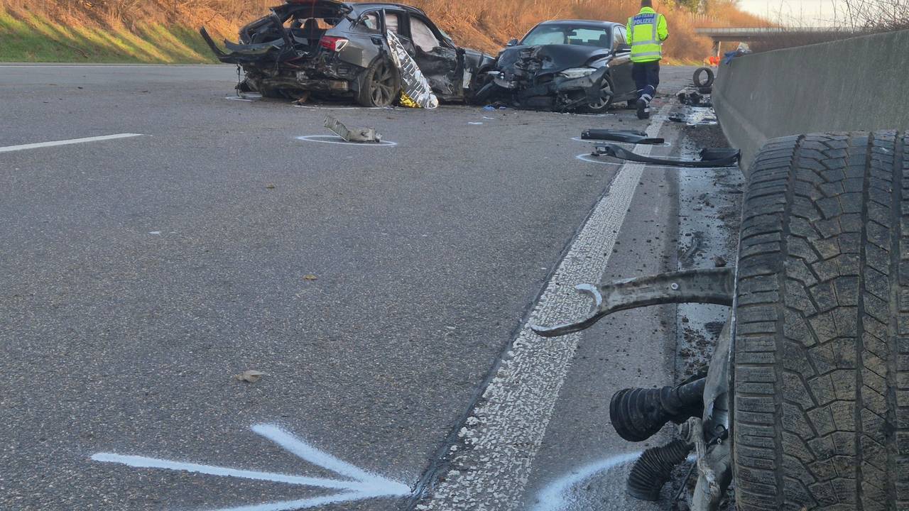 Ein Polizist geht nach einem Unfall auf der A1 an den verunglückten Fahrzeugen und zahlreichen Trümmerteilen entlang.