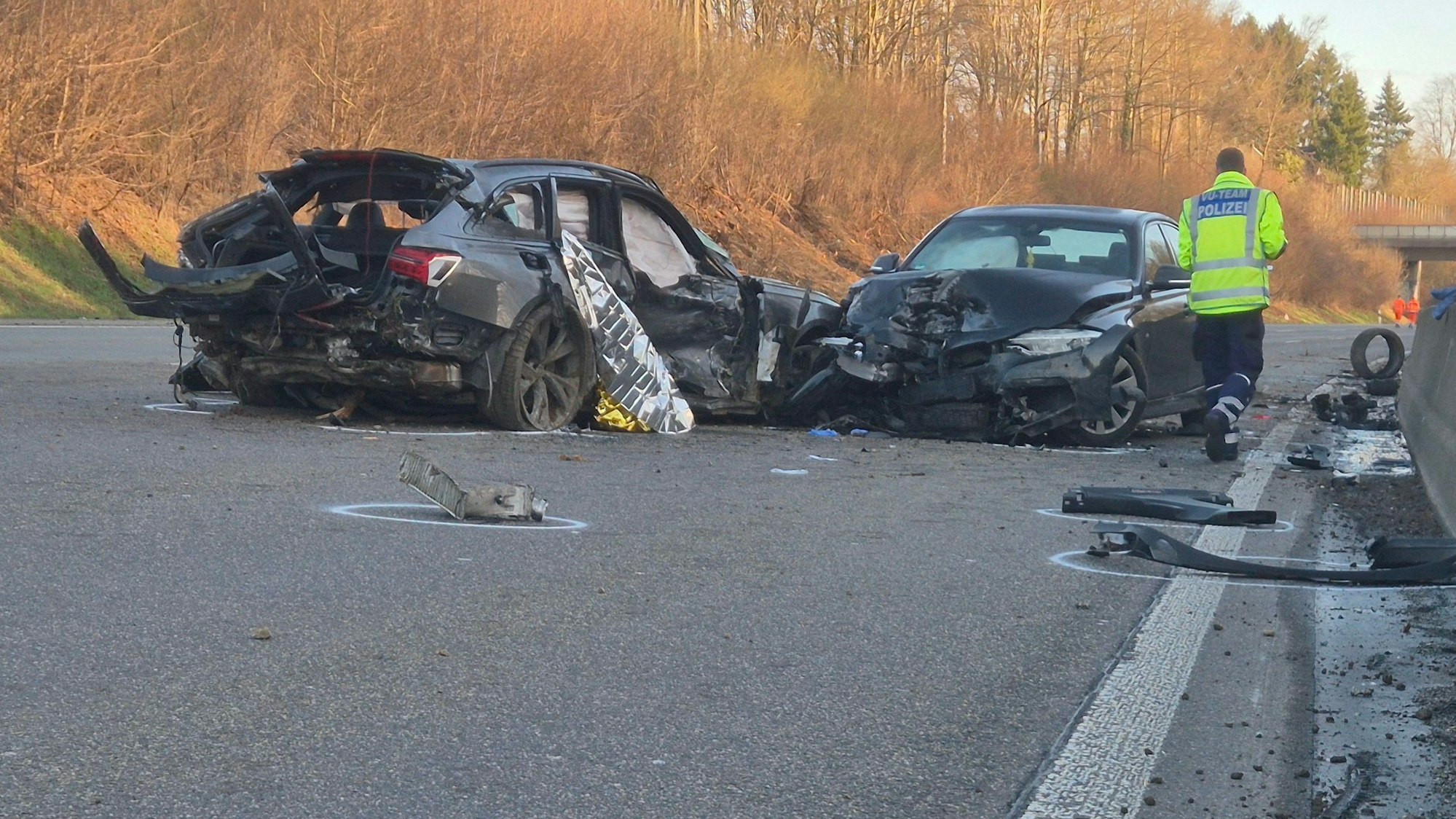 Ein Polizist geht nach einem Unfall auf der A1 an den verunglückten Fahrzeugen und zahlreichen Trümmerteilen entlang.