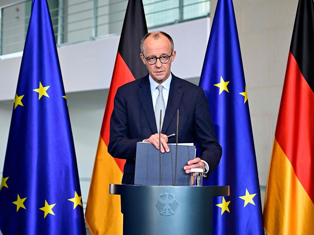 Bundeskanzler Friedrich Merz steht an einem Rednerpult, hinter sich jeweils zwei Deutschland- sowie EU-Fahnen.