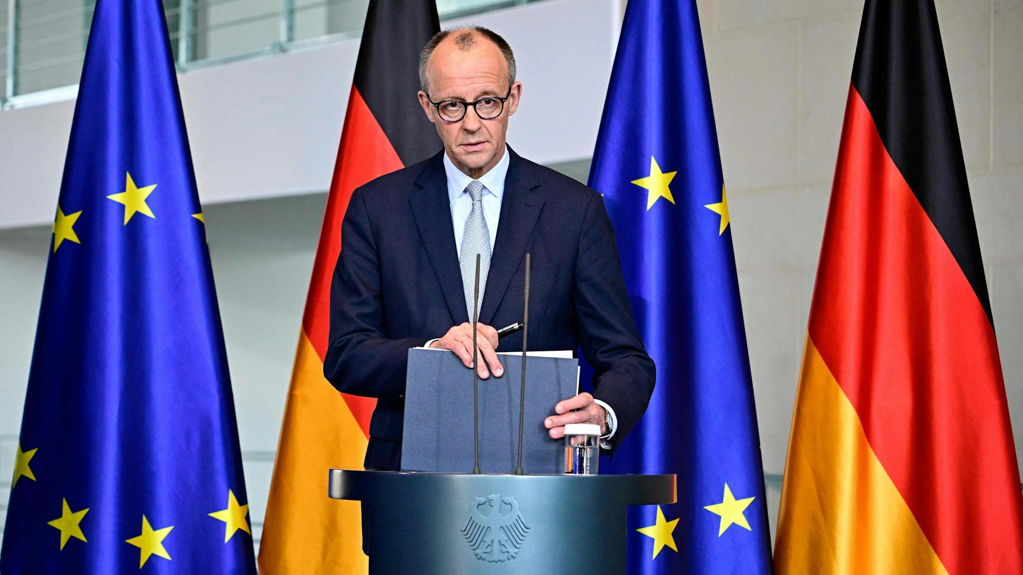 Bundeskanzler Friedrich Merz steht an einem Rednerpult, hinter sich jeweils zwei Deutschland- sowie EU-Fahnen.