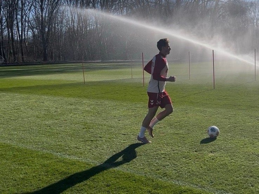 Sebastian Sebulonsen läuft über den Rasen. Vor ihm ein Ball, im Hintergrund läuft ein Rasensprenger.