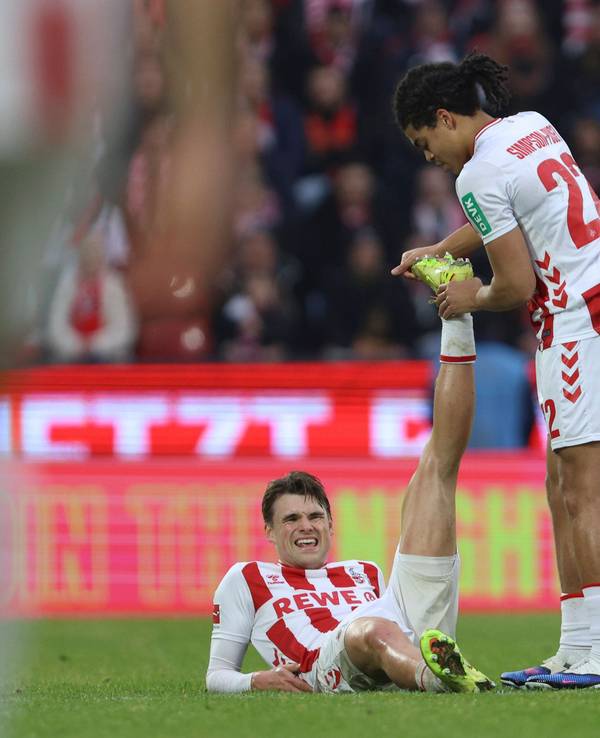 Joel Schmied (1. FC Köln) liegt verletzt am Boden, Jahmai Simpson-Pusey dehnt sein Bein.