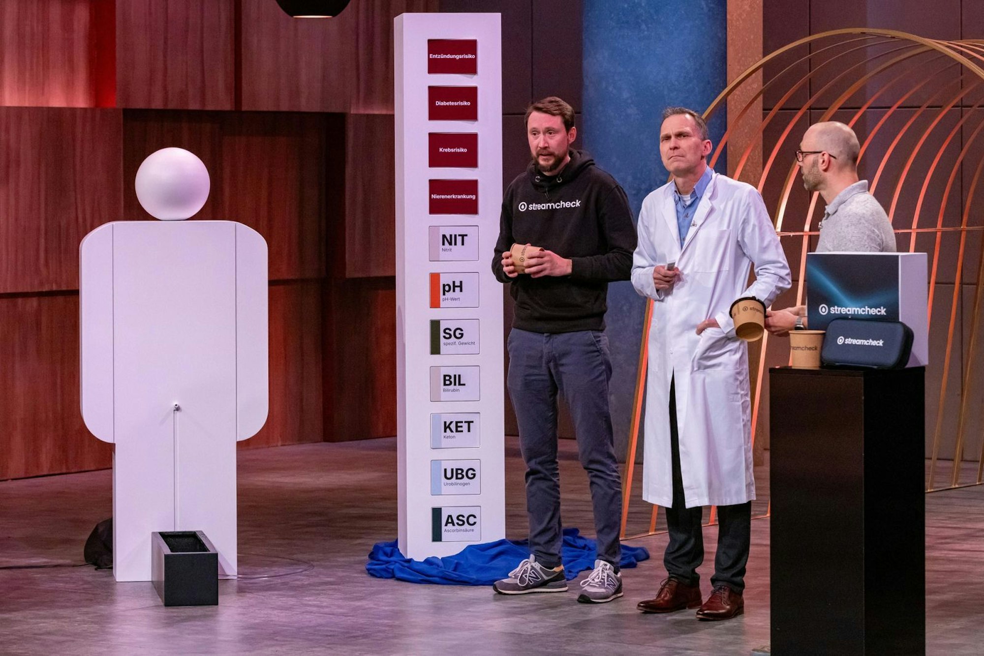 Ein Pappkamerad, der eine klare Sprache spricht: Das Gründertrio von „Streamcheck“ möchte erreichen, dass mehr Männer zu Hause ihren Urinfluss kontrollieren. (Bild: RTL / Bernd-Michael Maurer)