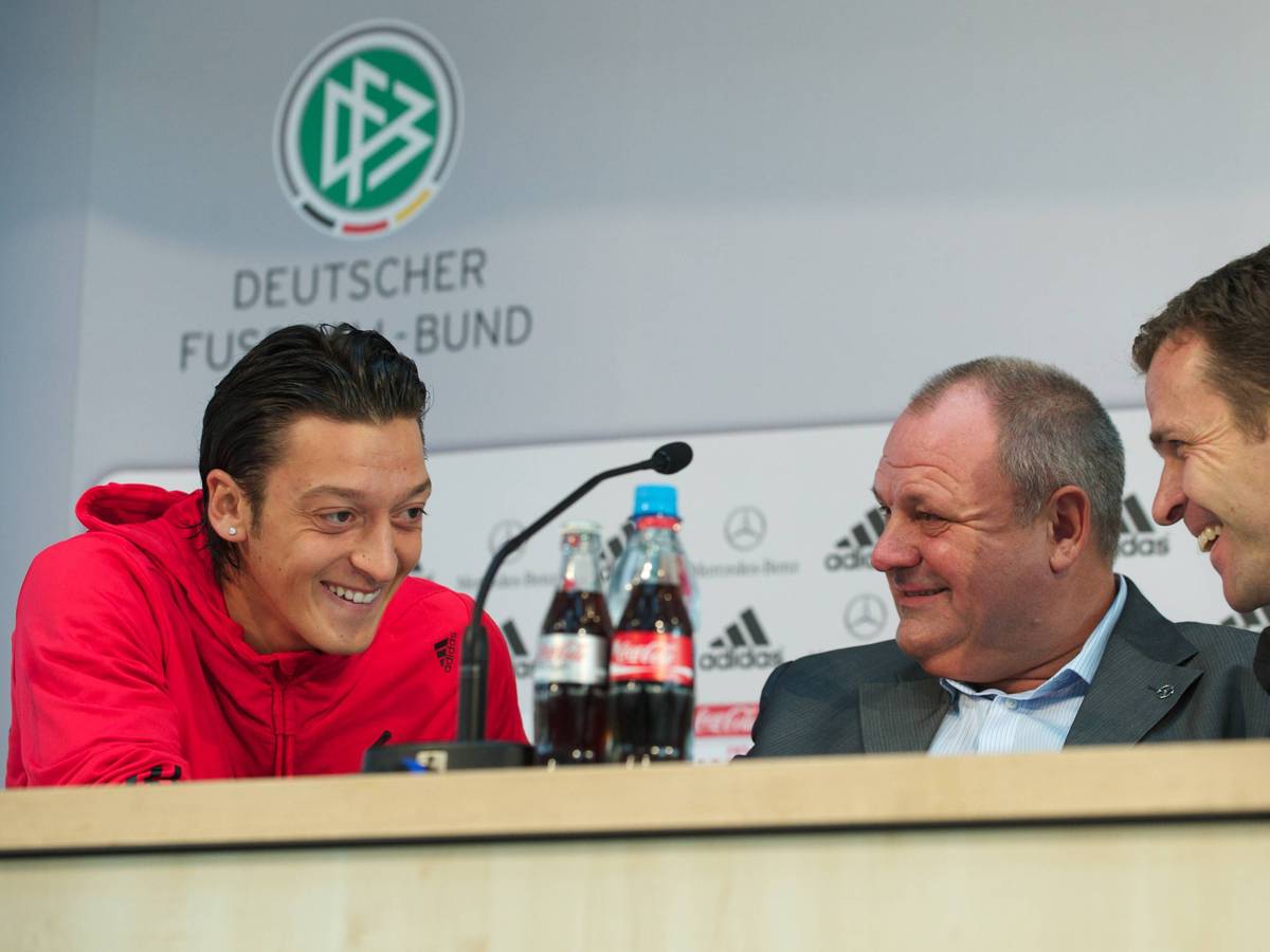 Mesut Özil, Harald Stenger und Oliver Bierhoff lachen bei einer Pressekonferenz.