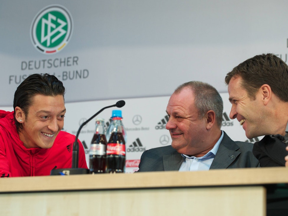 Mesut Özil, Harald Stenger und Oliver Bierhoff lachen bei einer Pressekonferenz.