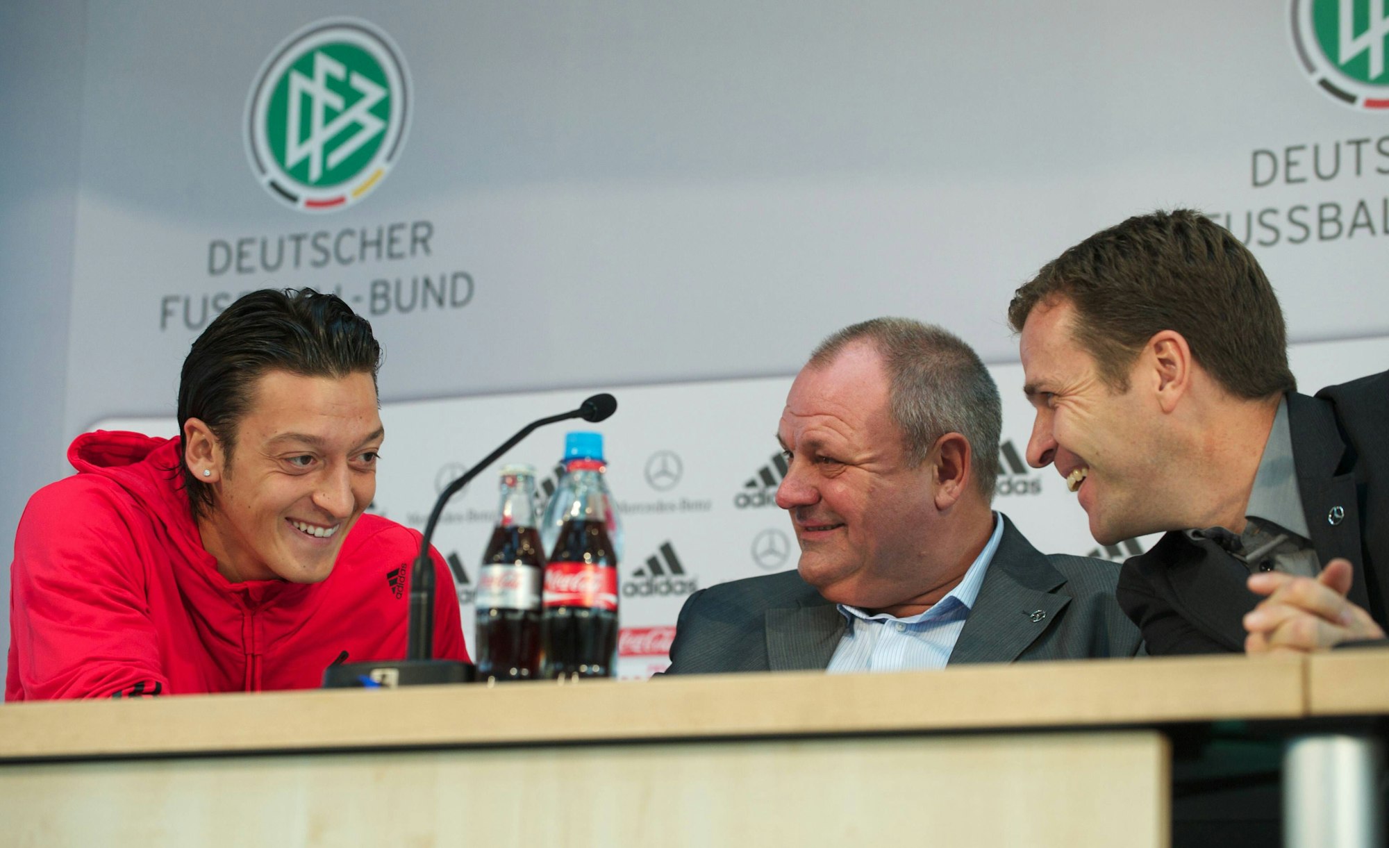 Mesut Özil, Harald Stenger und Oliver Bierhoff lachen bei einer Pressekonferenz.