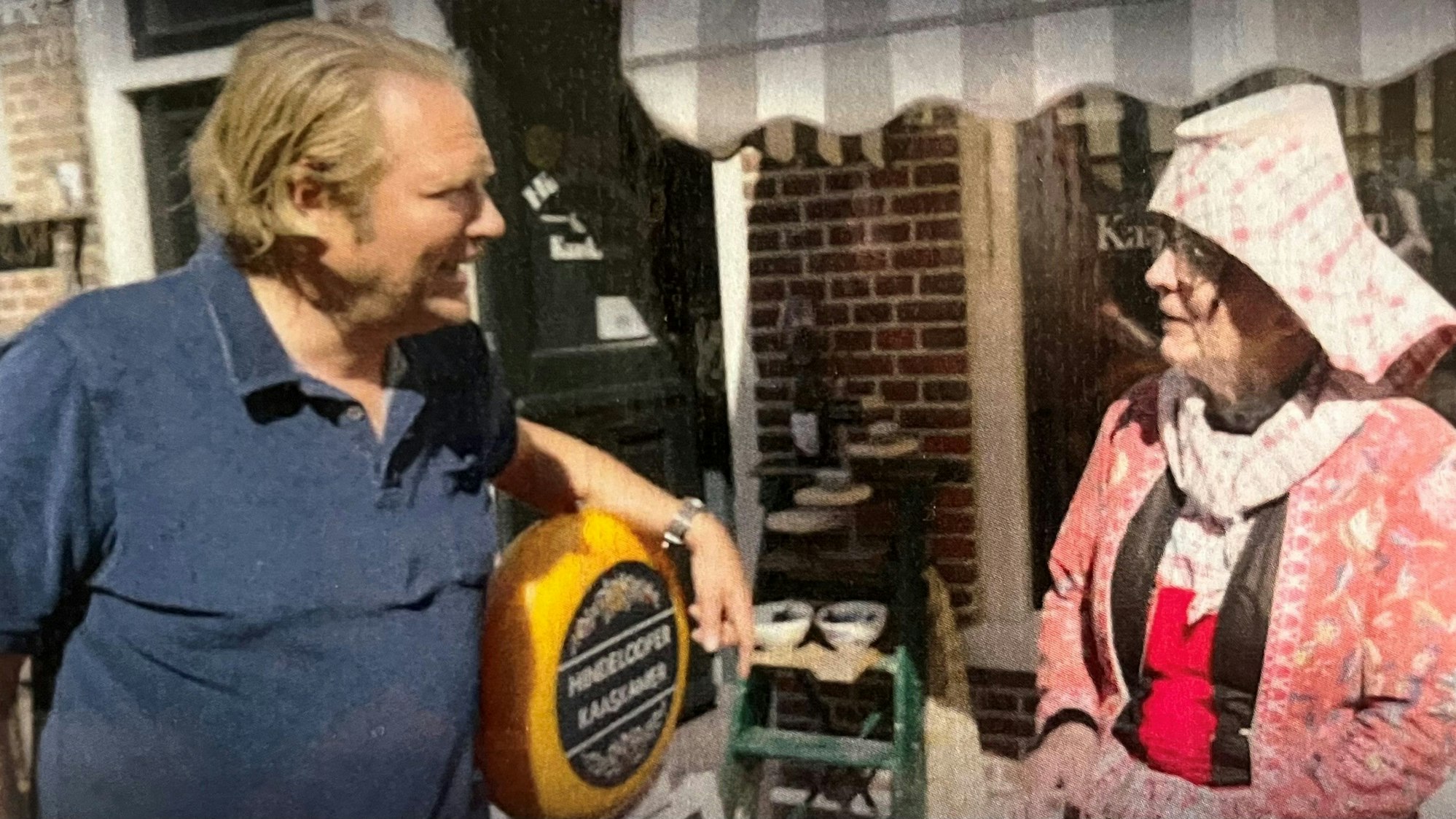 Ein Mann mit einem Käserad unterm Arm unterhält sich mit einer Frau in typisch holländischer Tracht