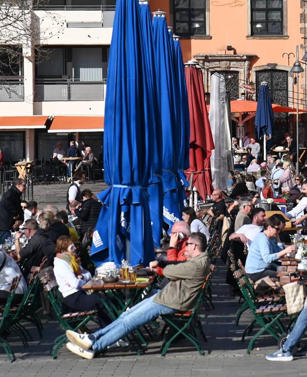 Menschen sitzen in einem Restaurant draußen und genießen die Sonne.