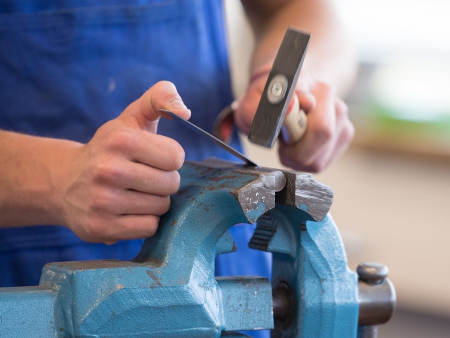 Auszubildender steht mit einem Hammer an einem Schraubstock