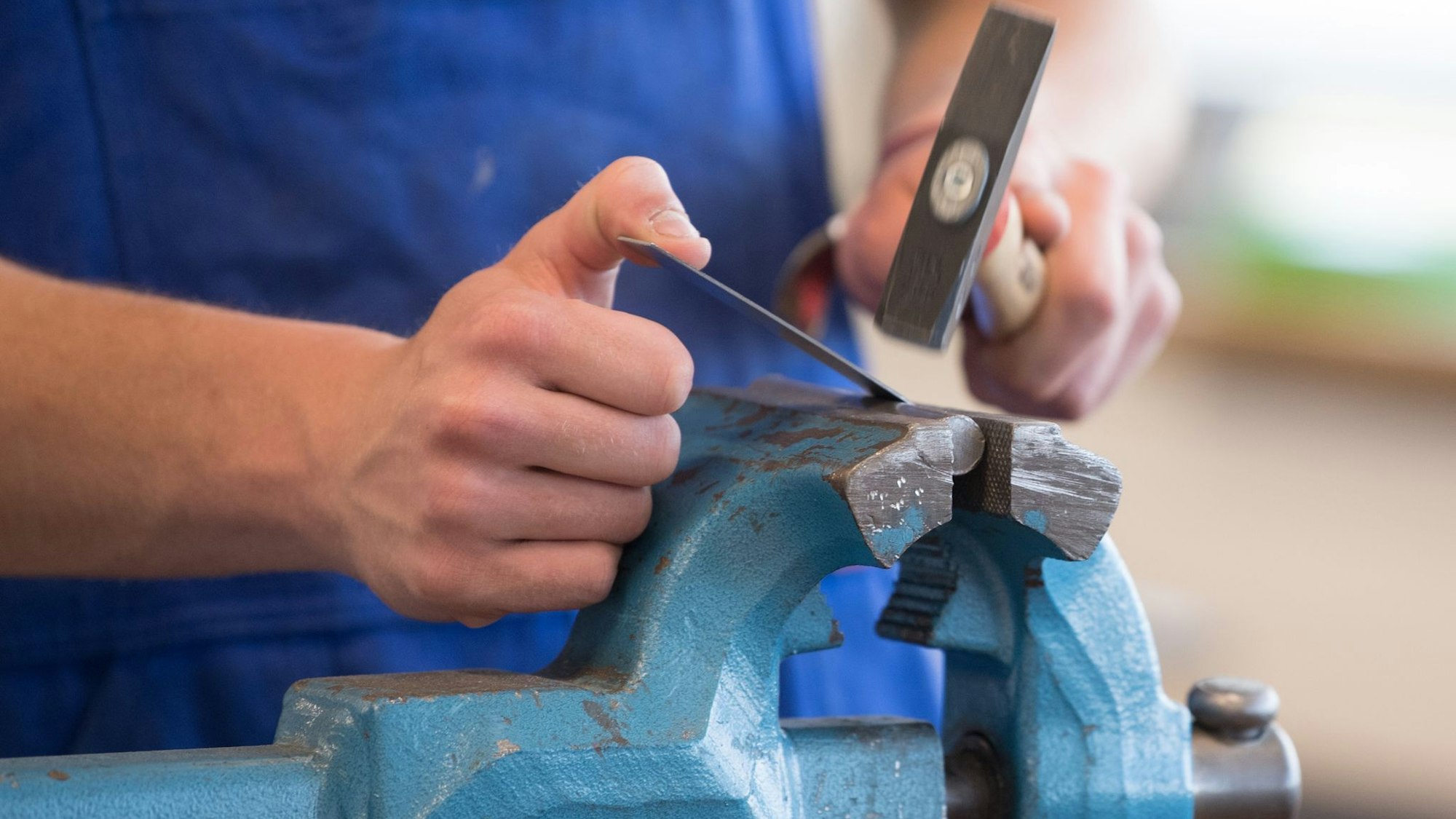 Auszubildender steht mit einem Hammer an einem Schraubstock