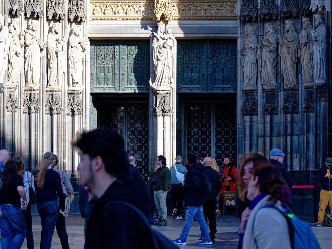 Touristen und Touristinnen passieren den Eingang zum Kölner Dom. Sie müssen in Zukunft Eintritt zahlen. Damit sollen die gestiegenen Kosten für Pflege, Schutz und den laufenden Betrieb des Doms gedeckt werden, wie das Domkapitel auf einer Pressekonferenz mitteilte.