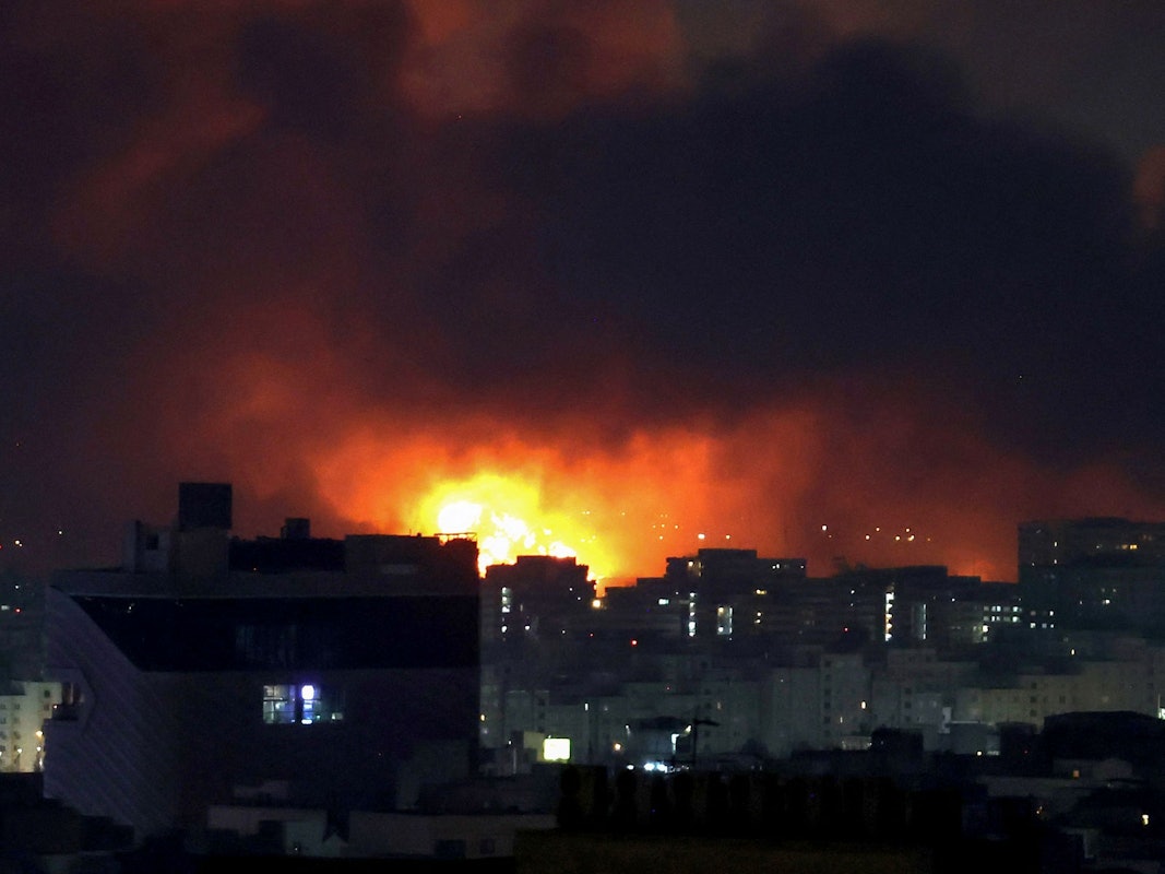 Hinter Häusern steigen in der Nacht Flammen auf.