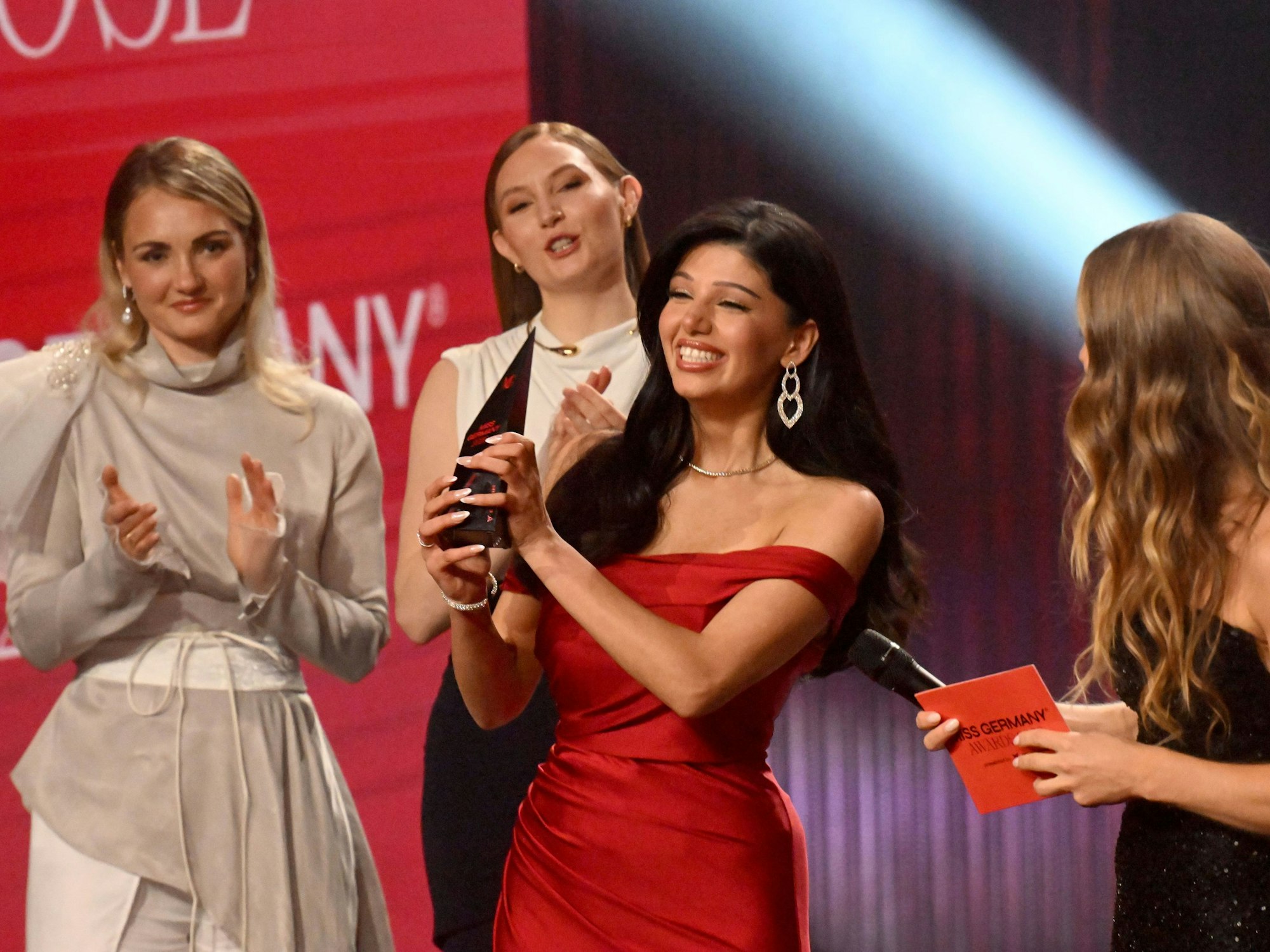 Rose Mondy ,Miss Germany 2026 (3.v.l) steht beim Finale "Miss Germany Awards" 2026 auf der Bühne im Bavaria Film Gelände als neue Miss Germany 2026 zusammen mit Amelie Reigl (2.v.l) und Anne Bäumler (l) und der Moderatorin Lola Weippert im Moment der Verkündung ihres Titels.