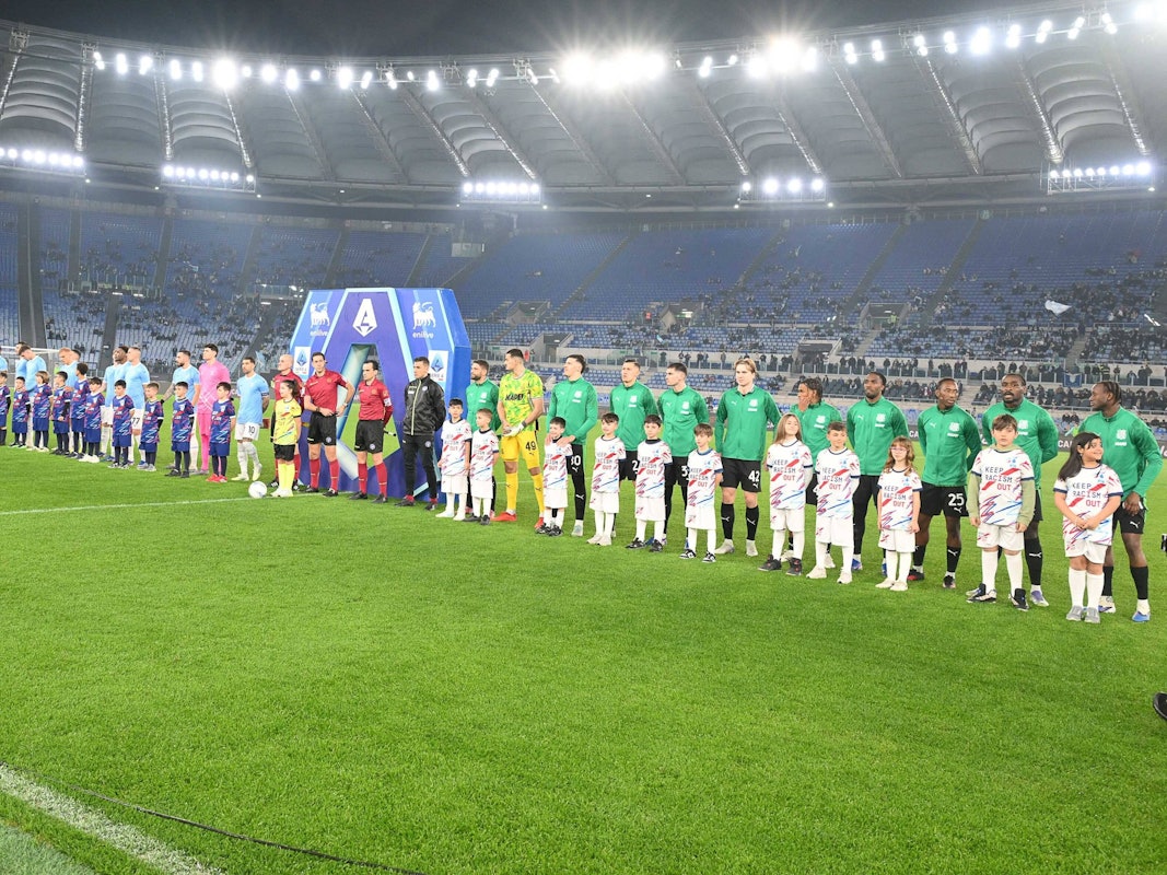 Die Mannschaften stehen vor dem Spiel aufgereiht, auf der Tribüne dahinter sind kaum Fans.