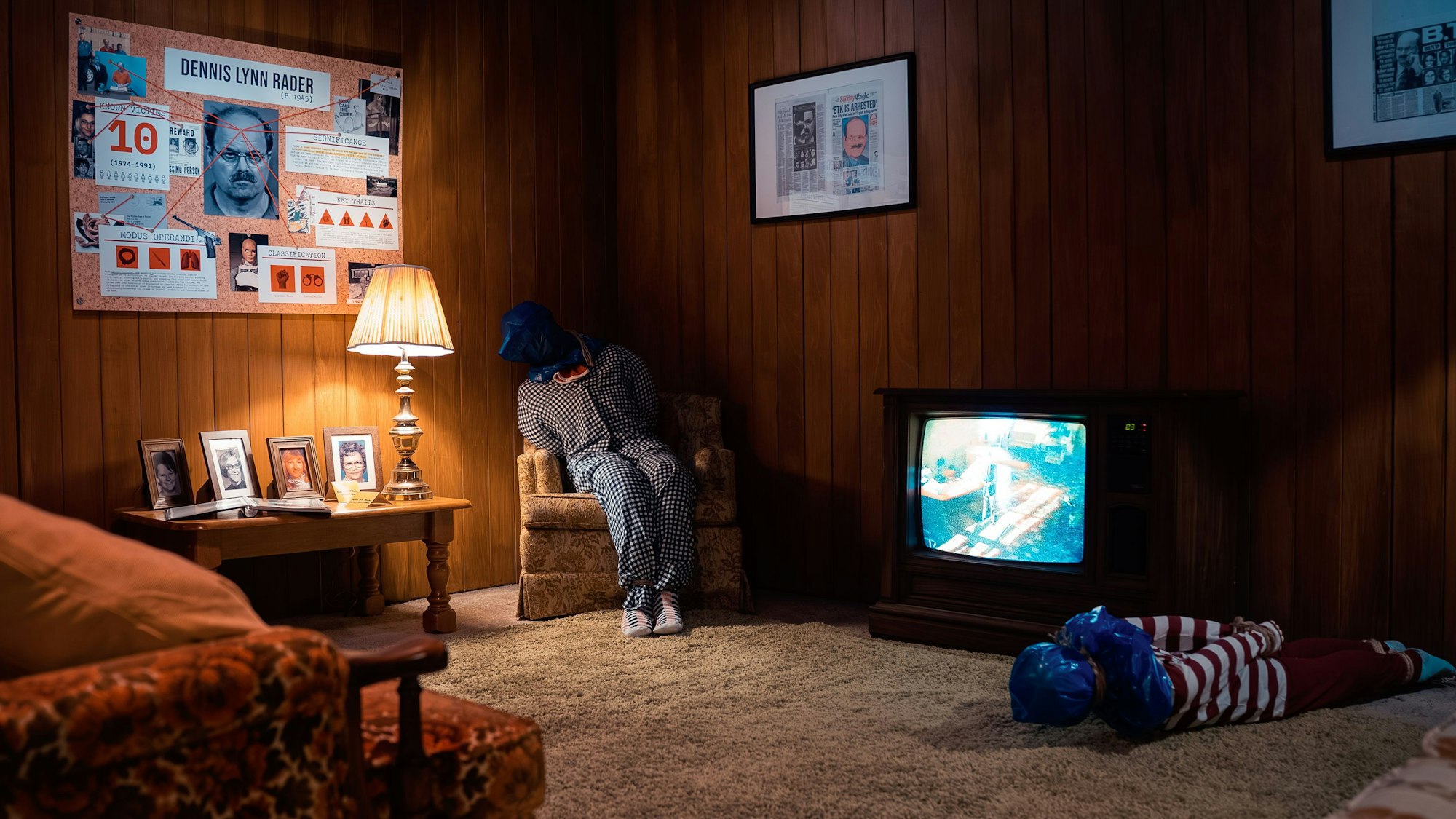 Eine Person sitzt gefesselt und mit einer Plastiktüte über dem Kopf auf einem Stuhl in einem Zimmer, vor ihr liegt eine weitere Person.