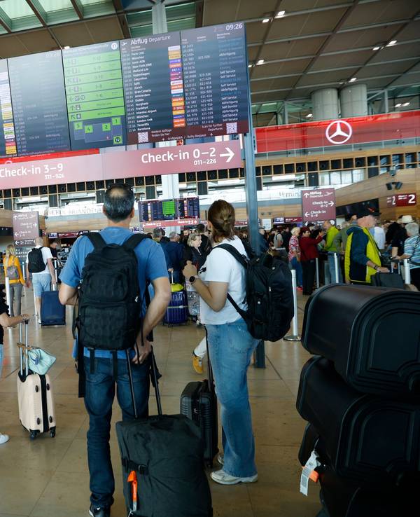 Reisende gucken auf eine Tafel am Flughafen.